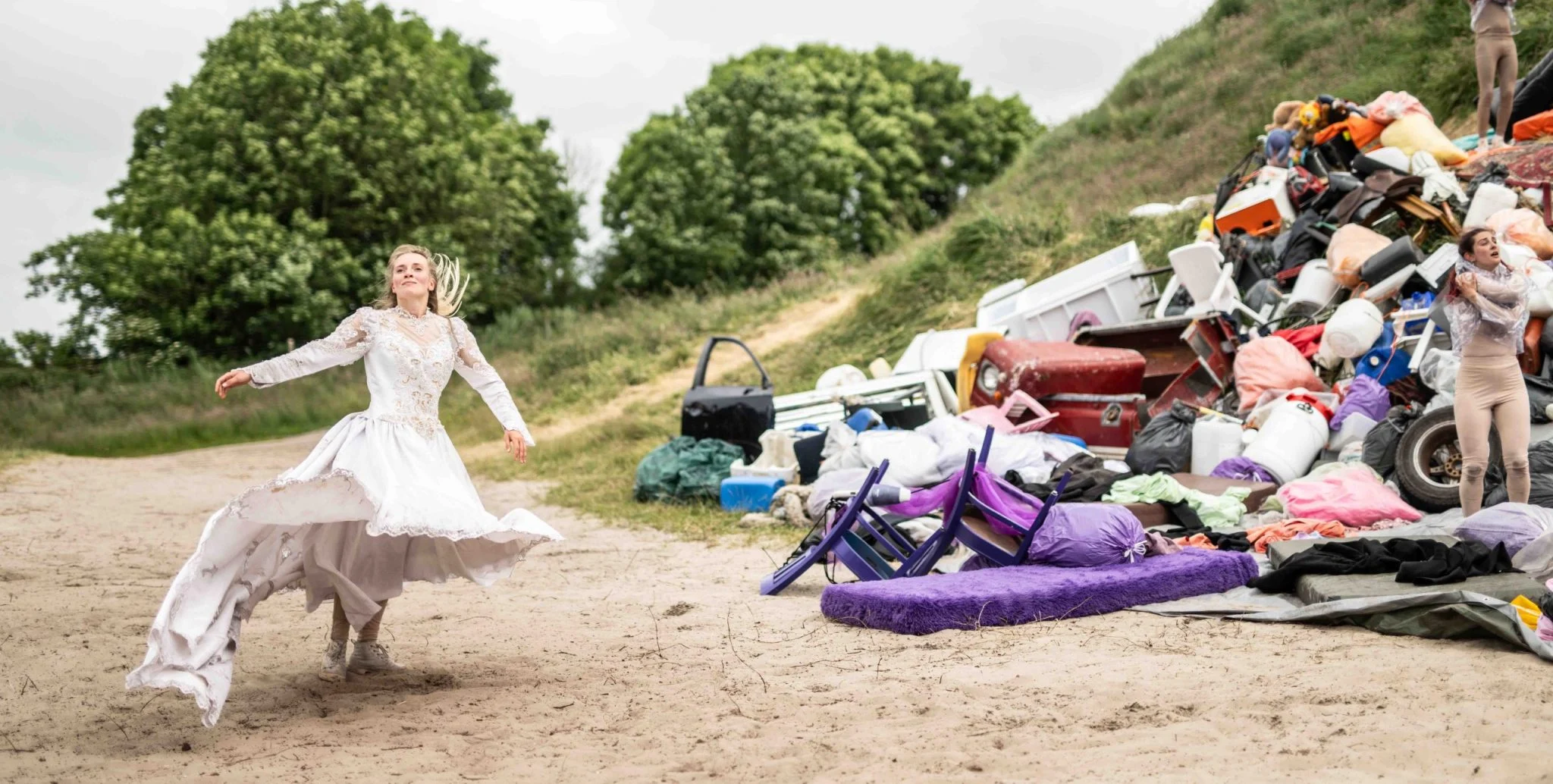 A dancer in a white dress on the beach, beside a heap of discarded objects