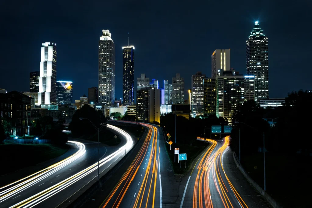Motorways with light trails of traffic alongside a lit skyline at night