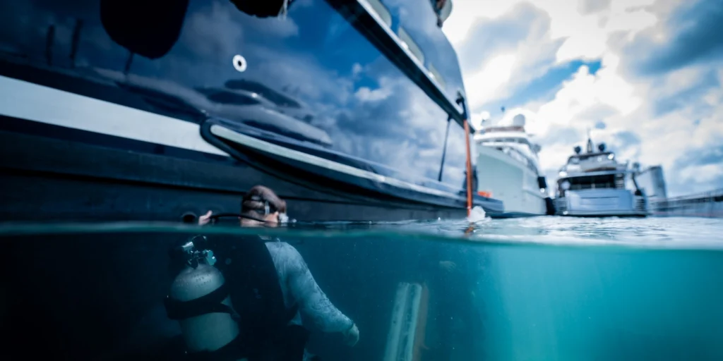 Photographed half below the waterline: a yacht floating above the submerged deck, with a diver underneath