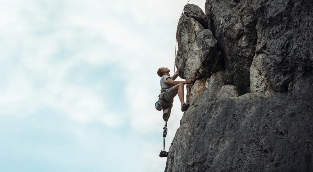 A climber with a prosthetic leg climbing up a rock face