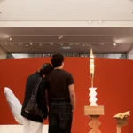 Twee bezoekers kijken naar een sculptuur voor een rode ronde wand in een museumzaal