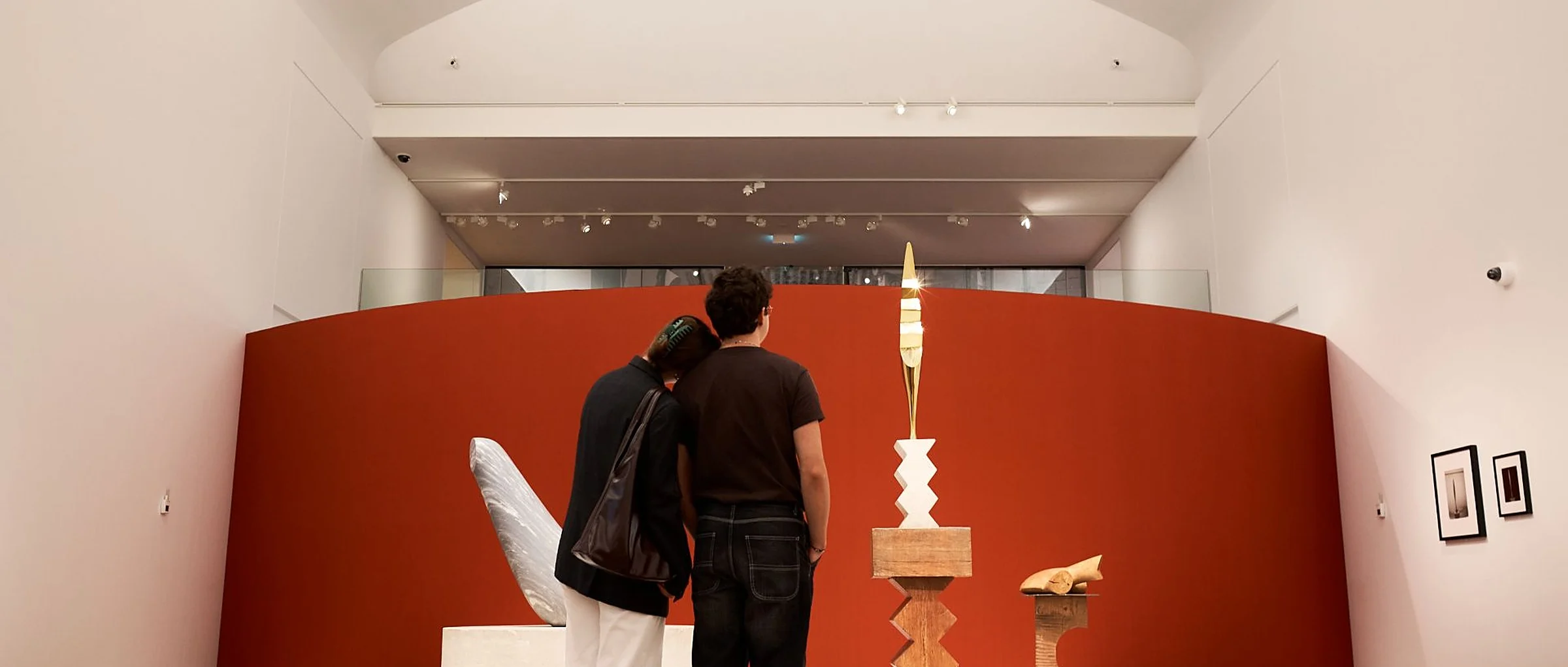 Two visitors looking at a sculpture in front of a round red wall in a museum gallery