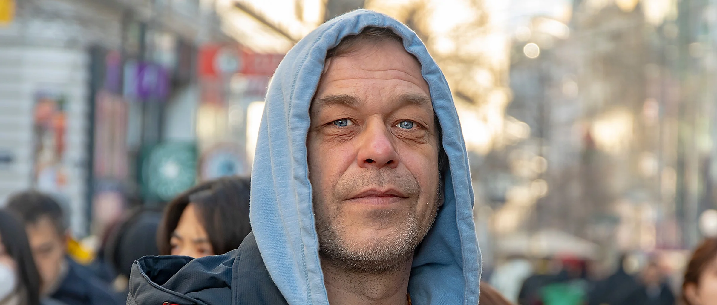 A man in a hooded top stands still in a busy shopping street