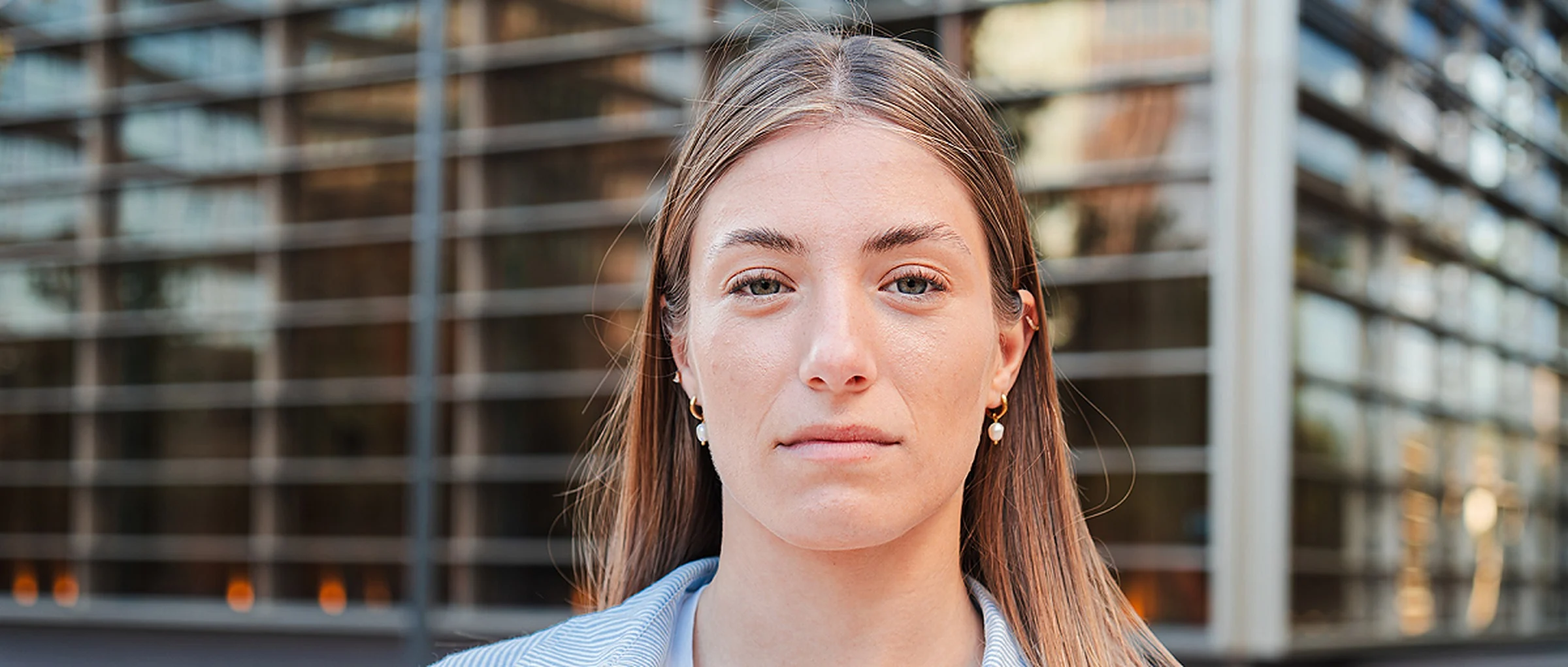 A young woman looks straight into the camera, with a building in the background